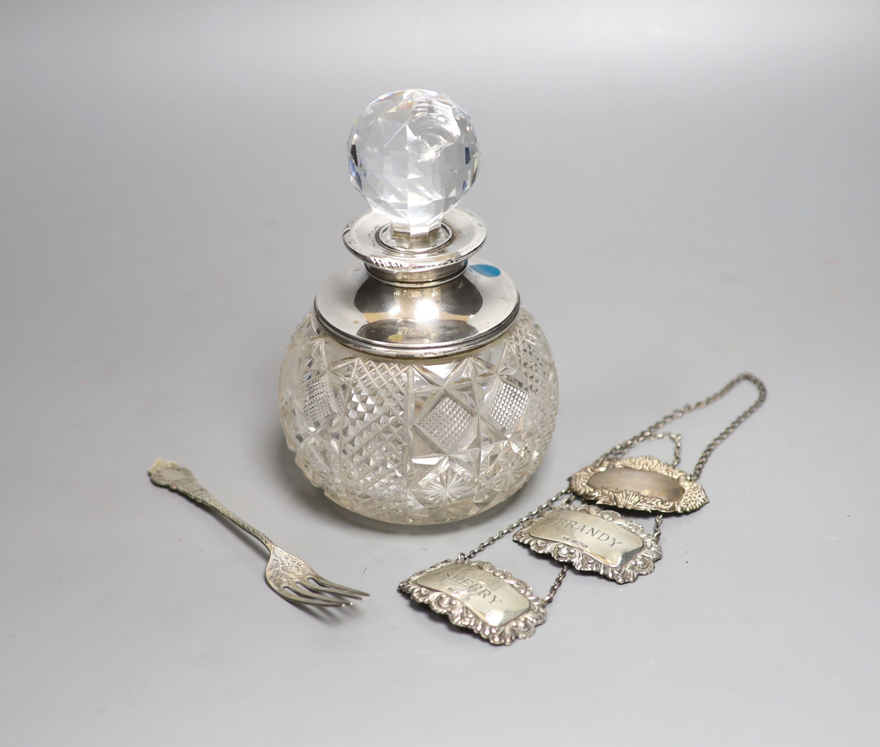 A George V silver mounted cut glass scent bottle with stopper, height 17.5cm, three modern silver wine labels and a silver fork.